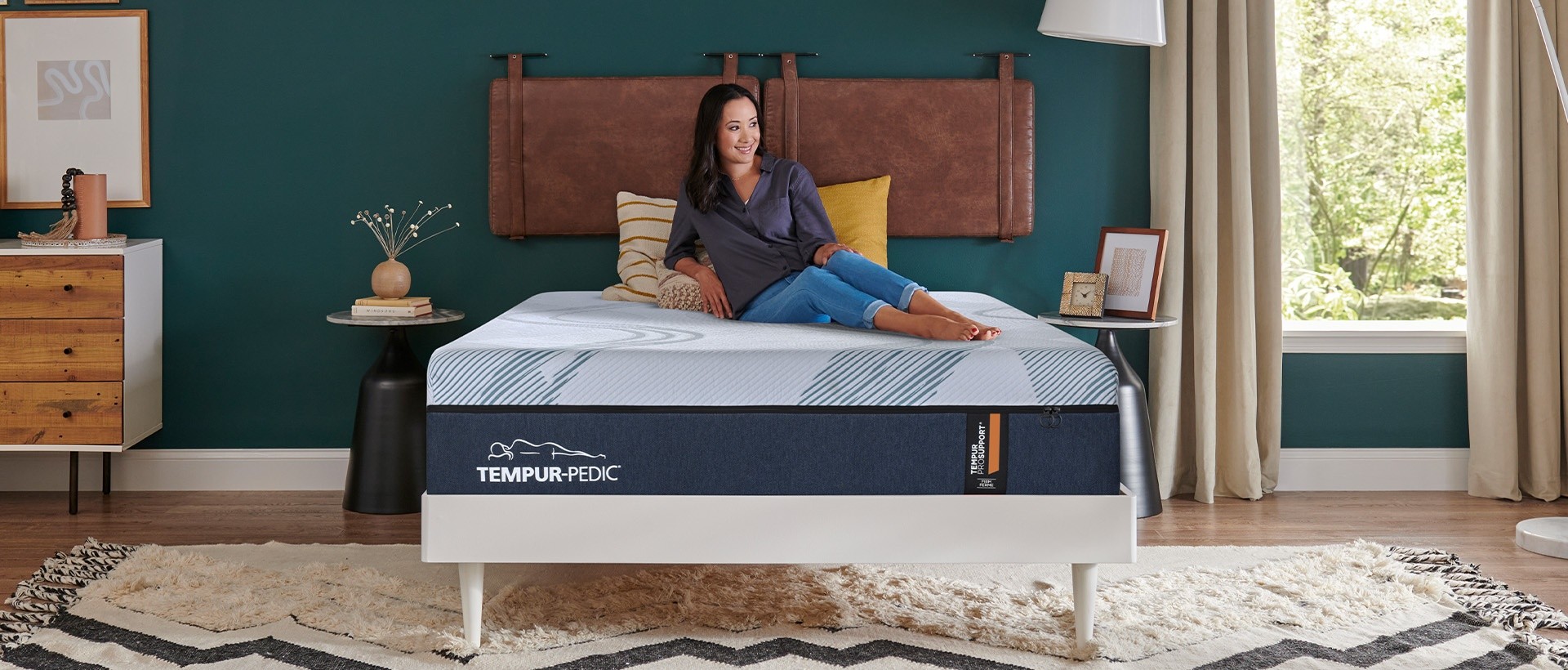 Woman smiling and lounging on a Tempur ProSupport firm mattress in a dark teal room