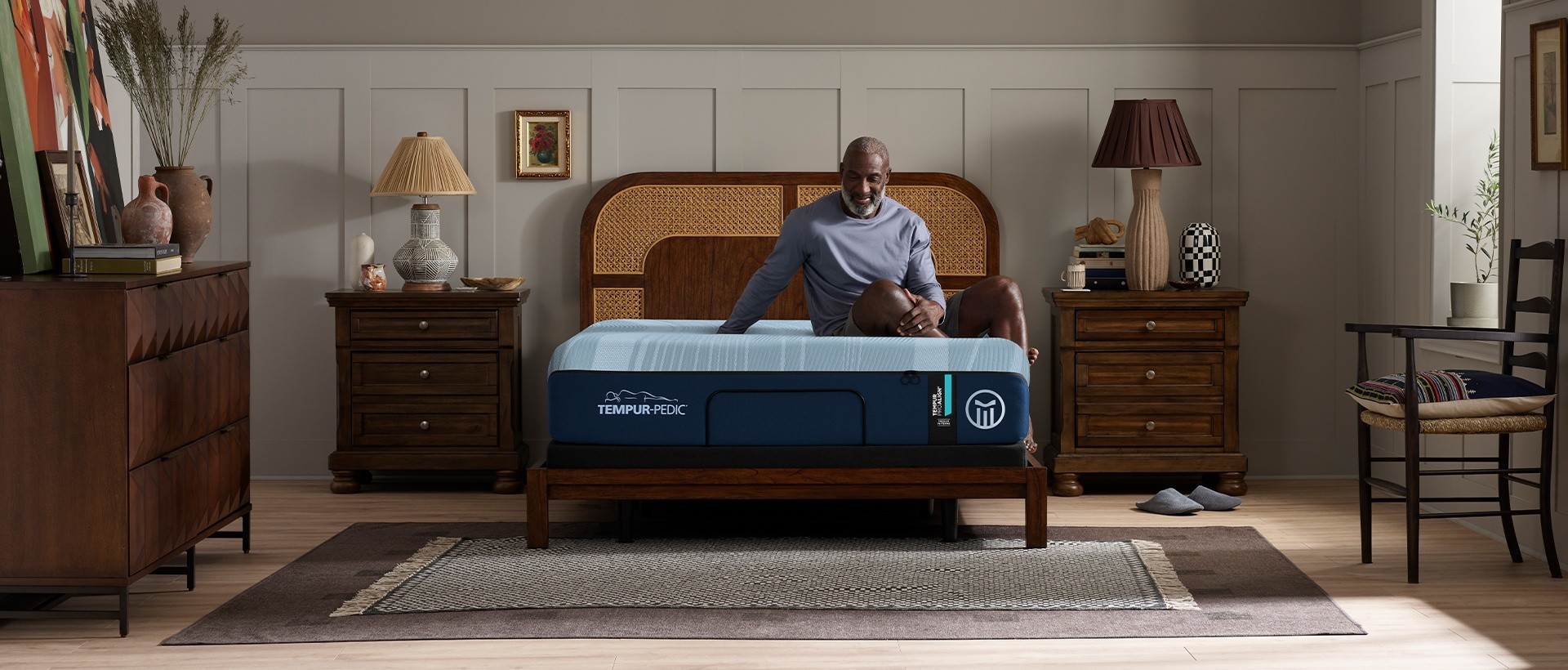 A man sitting calmly on a front-facing ProAlign mattress in a pleasant grey room