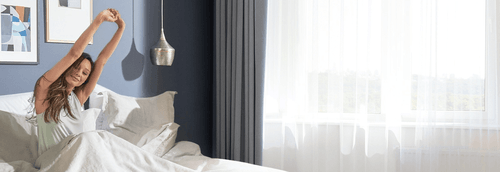 A woman in bed stretching waking up feeling refreshed after a great night sleep in a Tempur-Pedic mattress